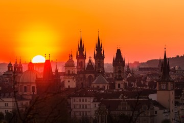 Fototapeta na wymiar View of orange and pink sky during morning sunrise in Prague, capital of the Czech Republic, sun shining behind black horizon with towers and spires, urban landscape