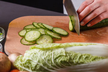 young woman in a gray apron cuts a cucumber