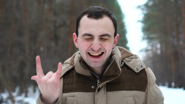 Portrait of handsome man in jacket is showing success gesture at camera. Man stands in winter forest
