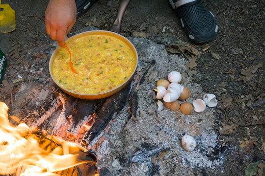 Male hand cooking Menemen or Omelette in pan on camping fire. Cook chep preparing traditional Turkish food as known Menemen. Selective focus.