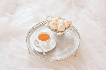 Silver tray with a cup of tea and macarons on a wooden white table in a white room