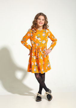 Fashion for girls 10 years in a yellow dress posing in the Studio. Curly hair, black shoes.
