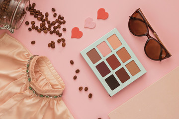 Women's dress, makeup shadows, diary and scattered coffee on a powdery pink background, flatlay, copyspase, closeup