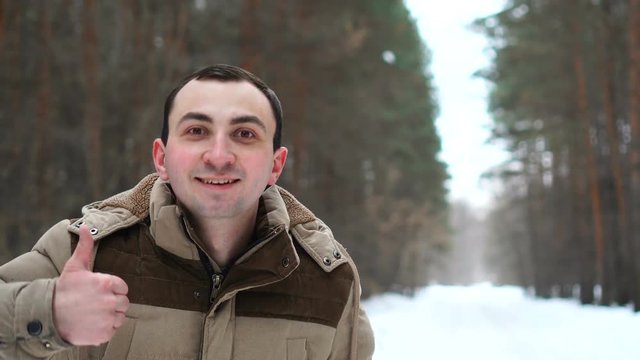 Portrait of man in a jacket is showing thumb up in winter forest