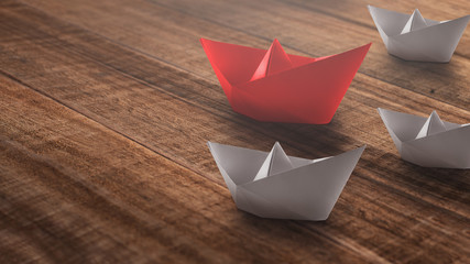 Leadership concept with red paper ship leading among the white on a rustic wooden background.