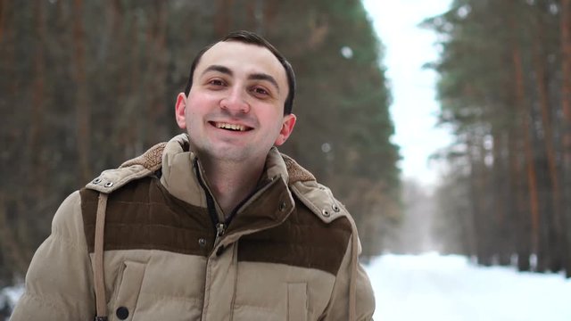 Portrait of young man in jacket is laughing with happy face. Man stands in winter forest