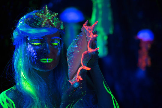 Water woman listening to a seashell .  Body art glowing in ultraviolet light. Neon