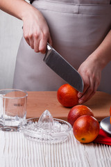 young woman in a gray apron cuts blood orange