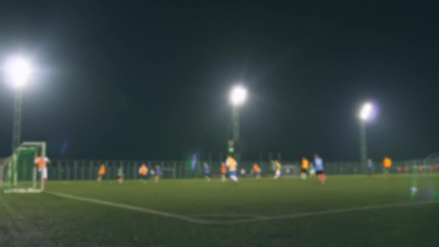 Evening football game. Football players play on the training field, illuminated by stadium lights. Blurred video.