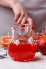 young woman in a gray apron squeezes juice of orange blood