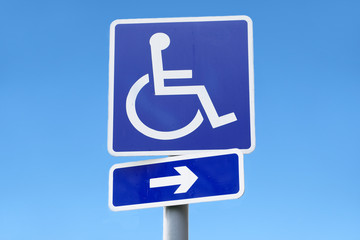 Disabled sign of wheelchair and direction arrow against empty clear blue sky