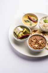 Indian vegetarian  platter / Thali having Palak paneer butter masala, dal makhani, flat bread or naan and rice served in a white plate