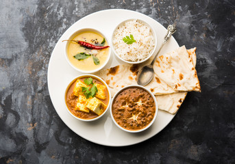 Indian vegetarian  platter / Thali having Palak paneer butter masala, dal makhani, flat bread or naan and rice served in a white plate