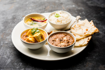 Indian vegetarian  platter / Thali having Palak paneer butter masala, dal makhani, flat bread or naan and rice served in a white plate