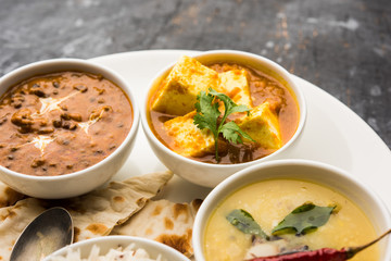 Indian vegetarian  platter / Thali having Palak paneer butter masala, dal makhani, flat bread or naan and rice served in a white plate