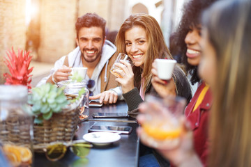 Group of international friends drinking coffee outside the coffee shop - Guy and girl smiling to their friends while chatting  during breakfast