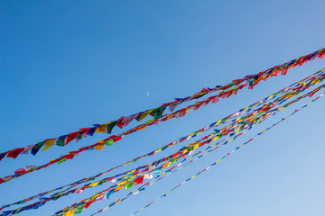 Buddhist Tibetan multicolored prayer flags against a clean blue sky and moon