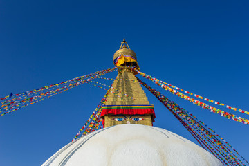 Buddhist Tibetan white stupa temple  Bodnath in Kathmandu with multicolored prayer flags against a clean blue sky