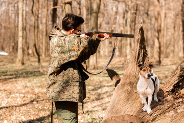Yang hunter with a dog on the forest. The hunter is aiming