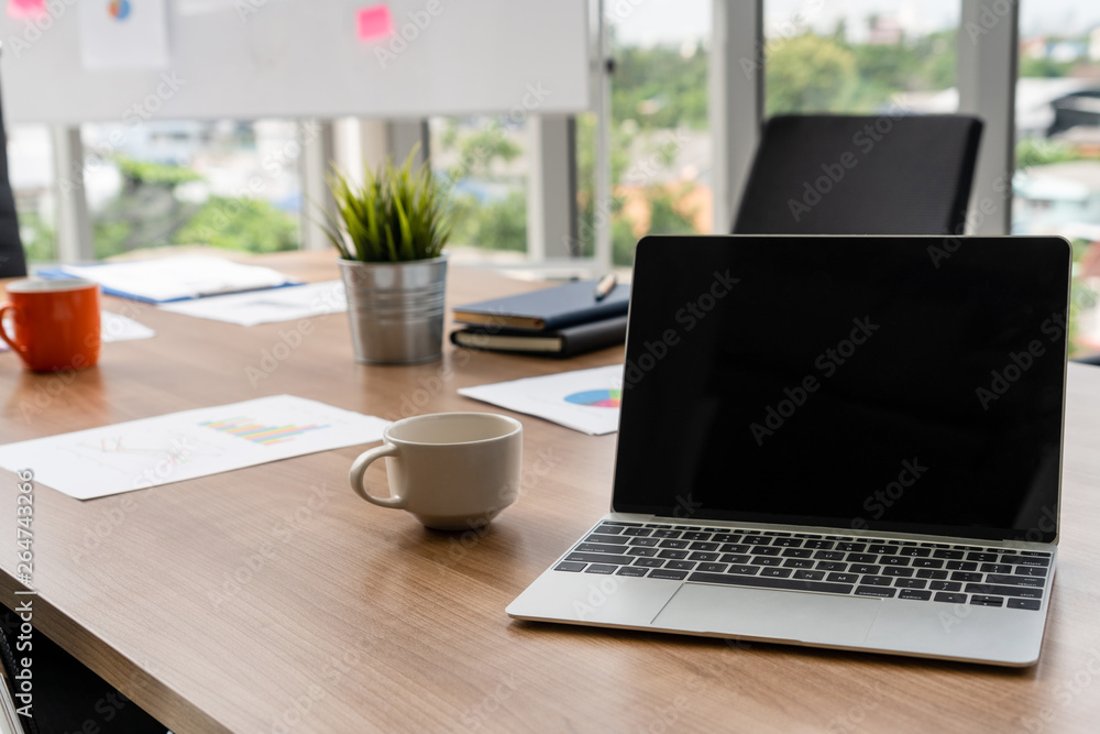 Poster laptop computer with opened lid on table in meeting room of office workspace.