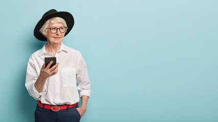 Half legth shot of stylish elderly female pensioner uses smartphone easily, being always in touch,...