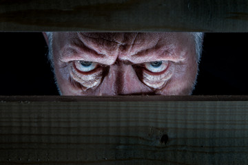 Portrait of a man looking evil from a hiding place. Concept evil, old man.