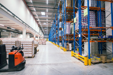 Warehouse storage facility interior. Large distribution center with shelves full of palette boxes and forklift machine.