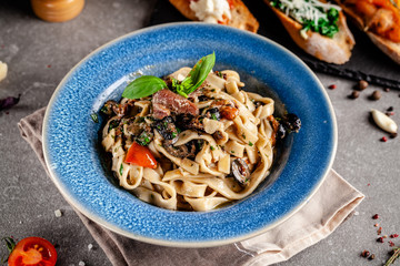 Concept of Italian cuisine. Pasta with anchovies, seafood and vegetables, olives, tomatoes and basil. Serving dishes in a restaurant in a blue plate. Background image. copy space