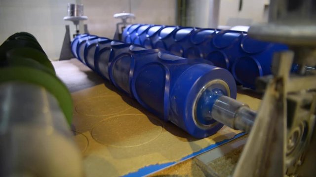 Static close up shot of cutter roller machine pressing circles into flat dough in bread making factory production line as circles move along conveyor belt.
