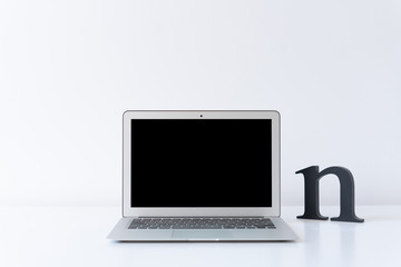 Open laptop and wooden black initial letter on the desk with white background