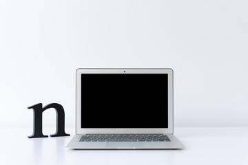 Open laptop and wooden black initial letter on the desk with white background