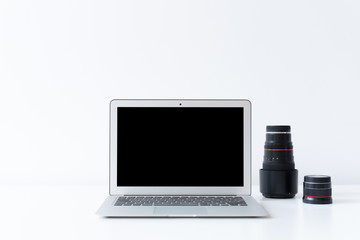 Open laptop and photography lenses on the desk with white background