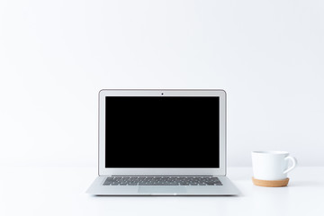 Open laptop and cup of coffee or tea on the desk with white background