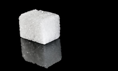 Cube of sugar on black reflective background.