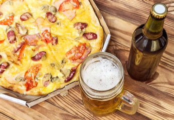 Glass of beer and pizza in pizza box on wooden table. Top view.