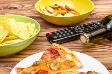 Beer with snacks and remote control for TV on the table.