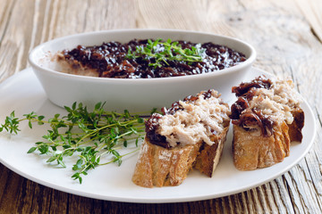 baguette slices with the pork rillettes and red onion confiture and a bowl with the pork decorated with thyme on the plate on wooden top 