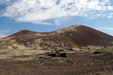 View over barren wide plain on red and green bare hills contrasting with blue sky and cumulus clouds - Iceland