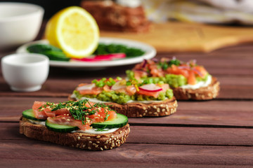 open sandwiches with rye bread smoked salmon cream cheese sliced cucumber dill avocado on wooden plank table  close up selective focus