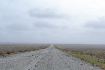 Wide old road in the foggy steppe