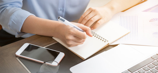 Business concept. Woman takes note for project with laptop and report in office desk. Backlighting, sun glare effect, close up, side view, copy space