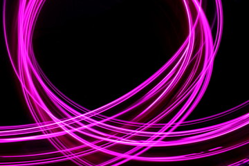 Fototapeta premium Long exposure, light painting photography. Vibrant neon pink loops and streaks of colour against a black background