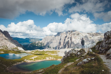 Fototapeta na wymiar Fotograf turysta stoi na skale nad górskimi jeziorami Tre Cime di Lavaredo w słoneczny dzień