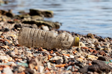 Obraz premium garbage on the river bank. discarded dirty plastic bottle with a yellow cap on the shore near the water. plastic pollution