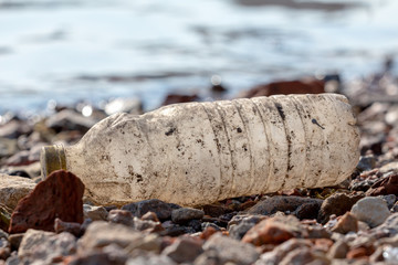 discarded dirty plastic bottle with a yellow cap on the shore near the water. plastic pollution