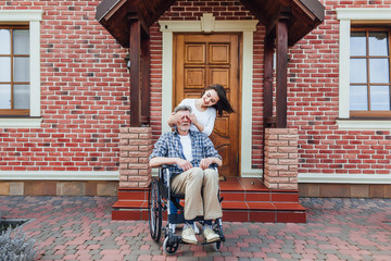 Happy young woman and her uncle on  wheelchair aoutdoors, Surprise for him.