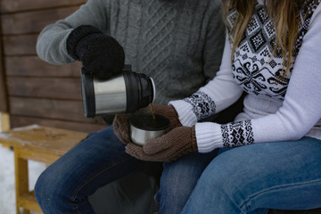 Fototapeta premium A pair of young children drinking tea from a thermos in the winter in the house, a Metal Cup from a thermos on the nature