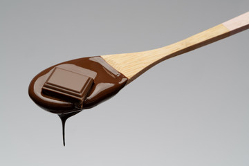 Liquid chocolate on a wooden spoon on light grey backgiund