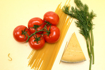 On a yellow background, red tomatoes on a green branch, a slice of yellow cheese, spaghetti pasta, dill twigs. Concept - healthy food. Top view