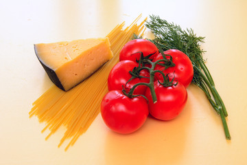 On a yellow background, red tomatoes on a green branch, a slice of yellow cheese, spaghetti pasta, dill twigs. Concept - healthy food